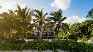 A beachfront property with a modern house, palm trees, and a sandy beach. - PRIVATE BEACHFRONT PARADISE with COOK & POOL = Luxury on the Sea! (San Pedro)
