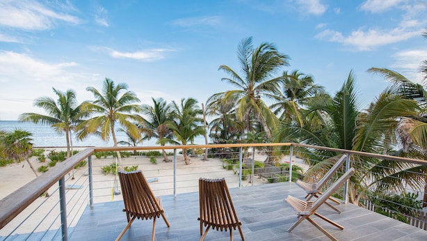 A balcony with two wooden lounge chairs overlooking a beach with palm trees and the sea. - PRIVATE BEACHFRONT PARADISE with COOK & POOL = Luxury on the Sea! (San Pedro)