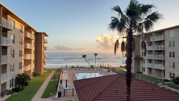 Un hotel frente a la playa con varios balcones, piscina y vistas al océano.
