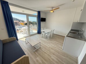 A modern room with a balcony, a dining table with chairs, a kitchenette, and a ceiling fan. - Agi Rescator 219 Apartamento for rent in Roses Girona. (Rosas / Roses)