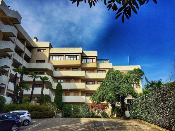 A multi-story residential building with balconies, surrounded by greenery and a parking area. - Cordelia 6 with lake view, balcony and pool (Luino)