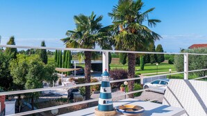 Ein Balkon mit Blick auf einen Garten, Palmen und ein geparktes Auto im Hintergrund.
