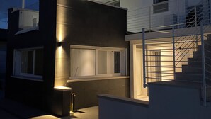 Ein modernes, zweistöckiges Haus mit einem Glasbalkon, einer Treppe und einer gut beleuchteten Außenfassade.