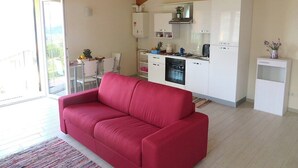 A modern kitchen with white cabinets, a red sofa, and a dining area with a table and chairs. - India apartment with lake view over Stresa (Stresa)