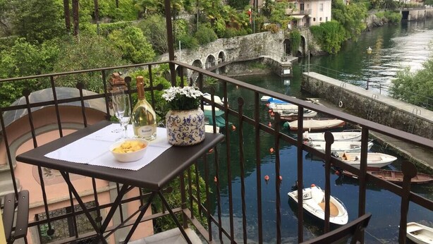 A balcony with a table set for dining, overlooking a river with boats and buildings in the background. - Casa al Vecchio Porto overlooking the ancient port (Cannero Riviera)