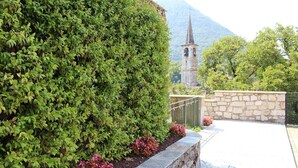 Un espace aménagé avec un mur en pierre, une clôture en métal et, en arrière-plan, le clocher d’une église.