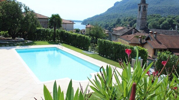 Une piscine entourée de verdure, une église et, au loin, une montagne.