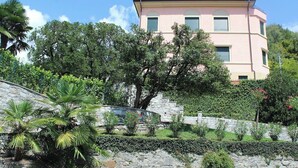 Un bâtiment rose avec un mur de soutènement en pierre et une végétation luxuriante.