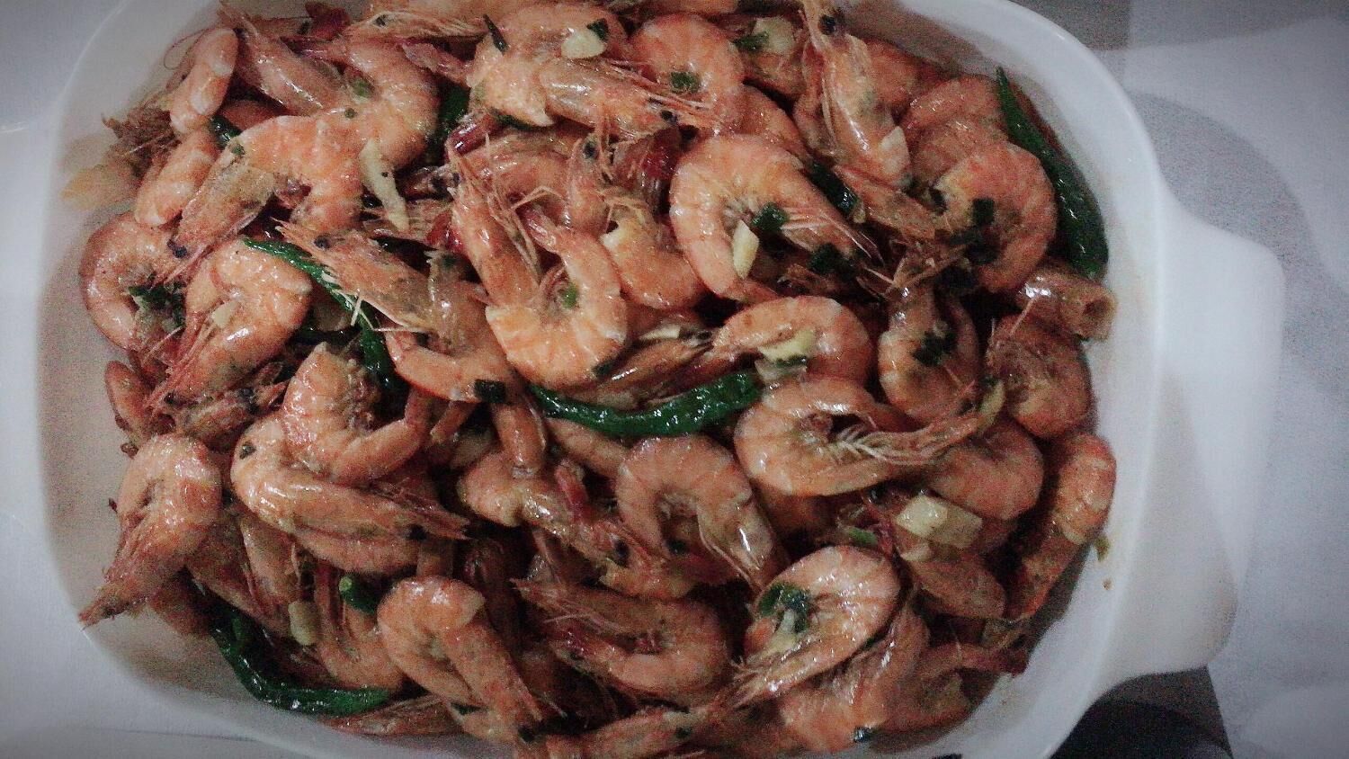 A dish of cooked shrimp with green chilies and herbs.