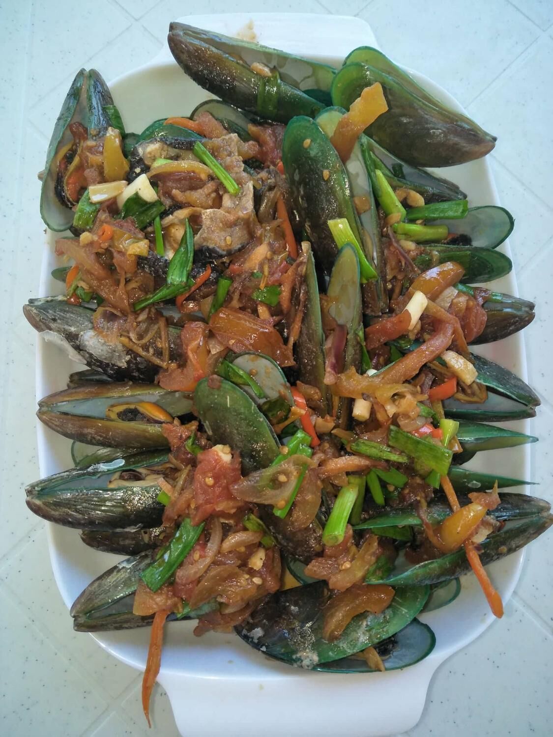 A dish of mussels with vegetables and sauce.
