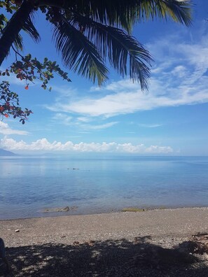Una playa con cielos despejados, agua tranquila y un barco a lo lejos.