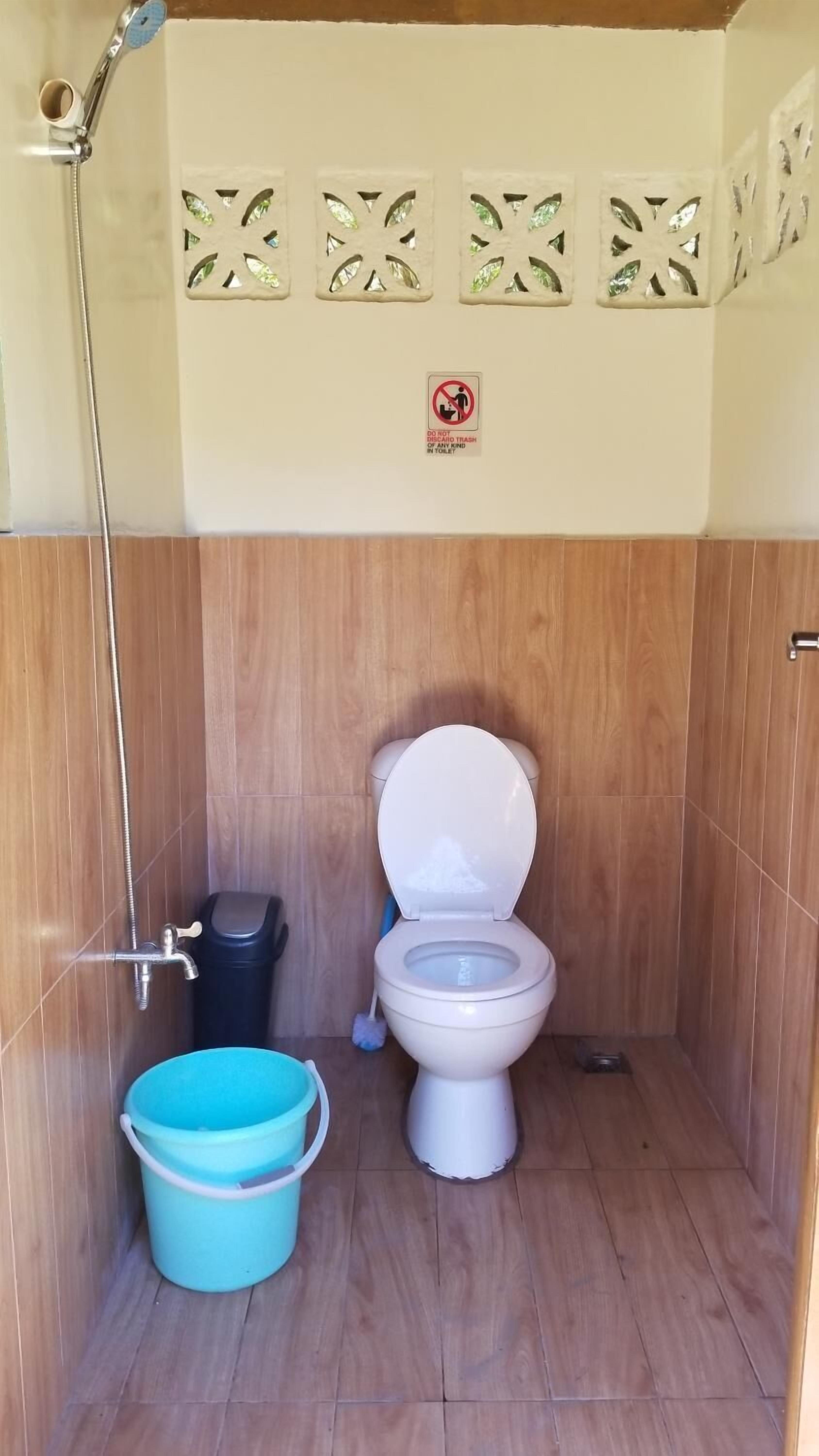 Un baño pequeño con inodoro, ducha y un cubo azul.