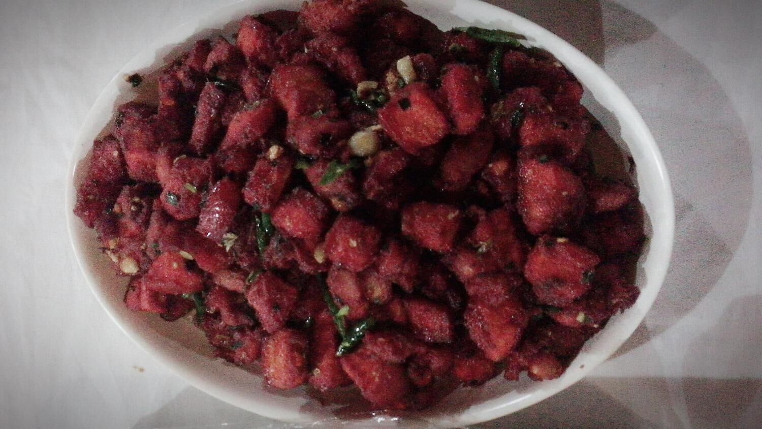 A bowl of food with a reddish-brown color, possibly a dish with chunks and herbs.