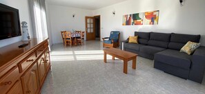 Un salon comprenant un canapé, une table basse, un téléviseur, une table à manger avec des chaises et des œuvres d’art accrochées au mur.