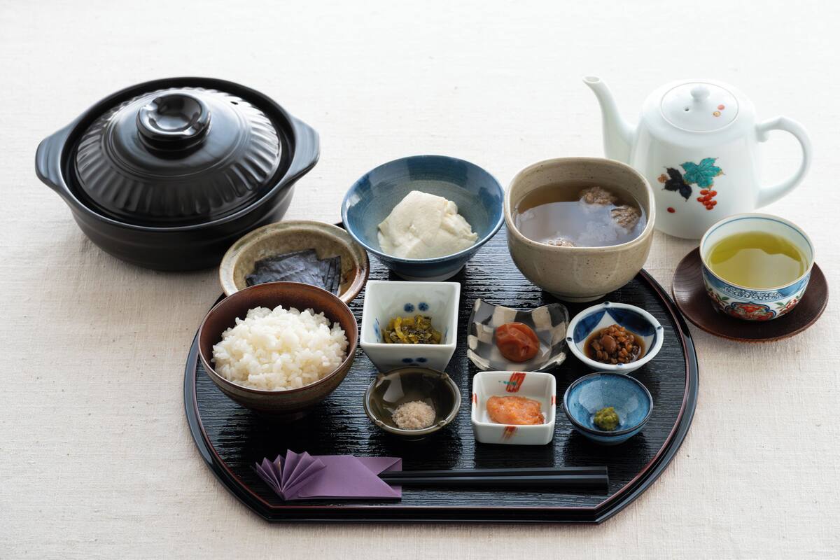 Una comida tradicional japonesa con una olla negra, arroz y diferentes pequeños platos sobre una bandeja.