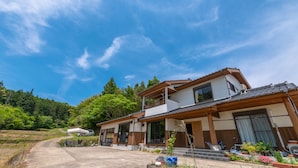 A two-story house with a large garage, a covered driveway, and a garden with various plants and flowers. - Share Creative&Bed 'adonoan' (Takeo)