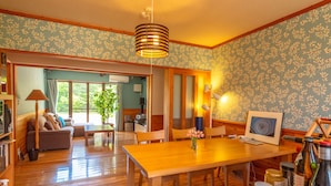 A spacious room with a wooden dining table, chairs, and a large window. - Share Creative&Bed 'adonoan' (Takeo)