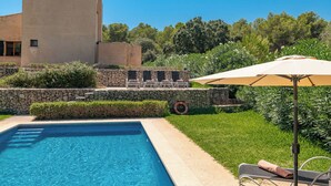 Une piscine avec un mur en pierre et des chaises longues.