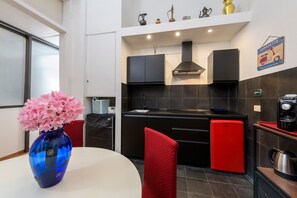 A modern kitchen with black cabinets, a red refrigerator, and a blue vase with flowers on the table. - Babuino Superior - Spanish steps (Roma)