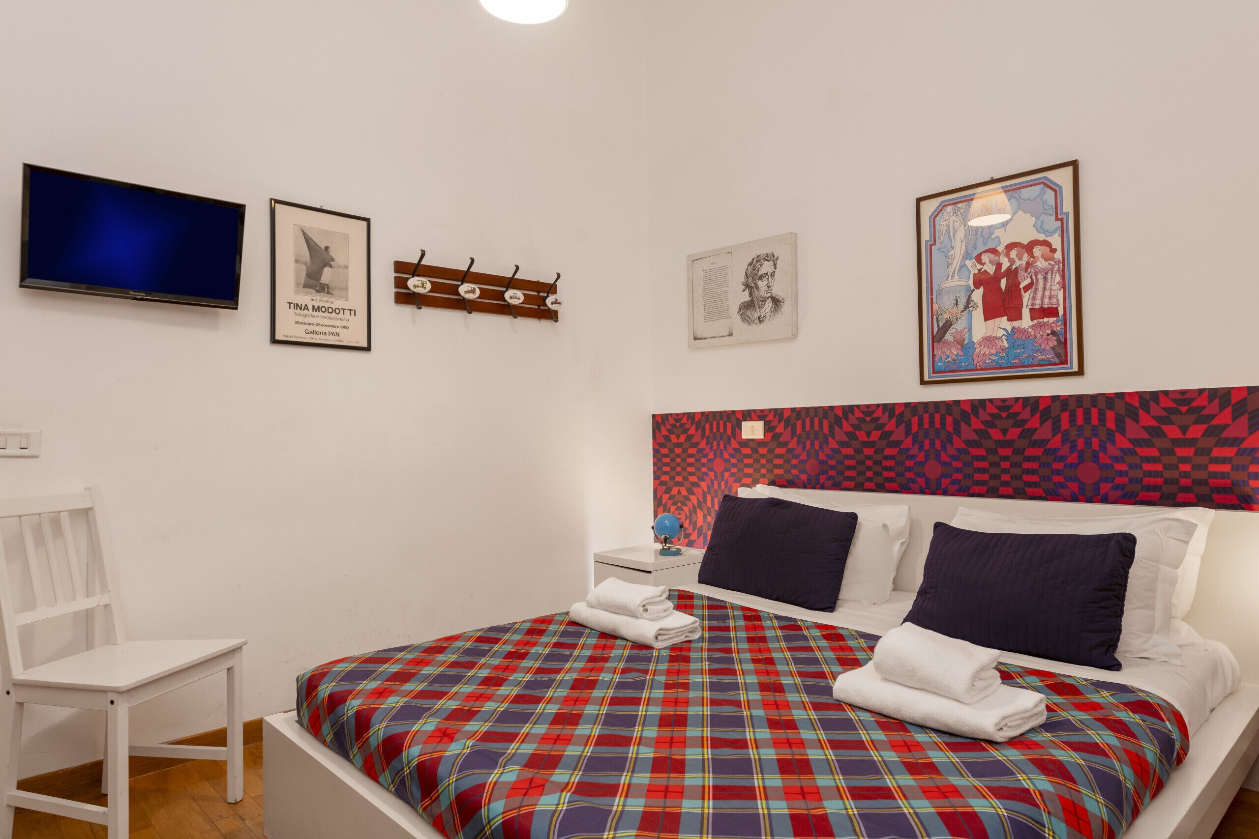 Une chambre d’hôtel avec un lit, une chaise, une télévision et des œuvres d’art accrochées aux murs.