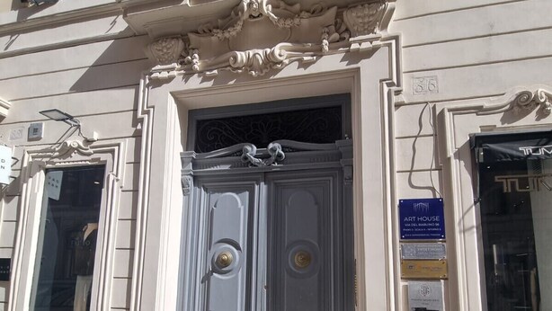 A building with a large, ornate entrance door, a sign indicating an art house, and a visible manhole cover on the sidewalk. - Babuino Superior - Spanish steps (Roma)