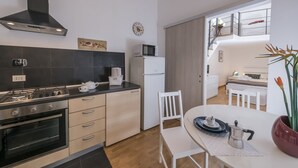 A modern kitchen with a stove, oven, and microwave. There is a dining area with a table, chairs, and a vase with flowers. - Babuino Superior - Spanish steps (Roma)