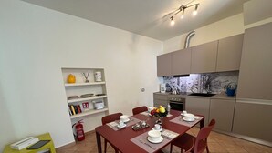Een compacte keuken met moderne apparaten, een eettafel voor vier personen en een klein boekenrek met decoratieve objecten.