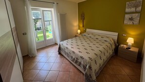 Een slaapkamer met een bed, twee bedlampen, een plafondventilator, een raam met gordijnen, een radiator en een muur met twee schilderijen.