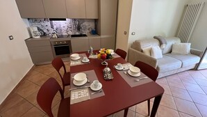 Een compacte keuken met moderne apparatuur, een eettafel voor vier personen met een rode tafelkleed, en een gezellig woongedeelte met een bank en een raam.