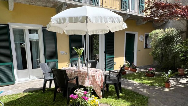 Een terras buiten met een tafel, stoelen, een witte parasol en potplanten.