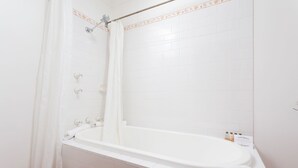Un baño blanco con bañera, azulejos blancos y una cortina de ducha.