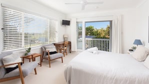 Habitación de hotel con una cama grande, un escritorio, dos sillas, un televisor y un balcón con vistas a zonas verdes.