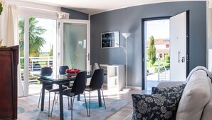 A modern living room with a glass dining table, black chairs, a grey sofa with floral cushions, and a view of the outdoors through large sliding glass doors. - Country villa app. with POOL, A/C,WIFI, PARK and 28sqm PRIVATE TERRACE. (Casalserugo)