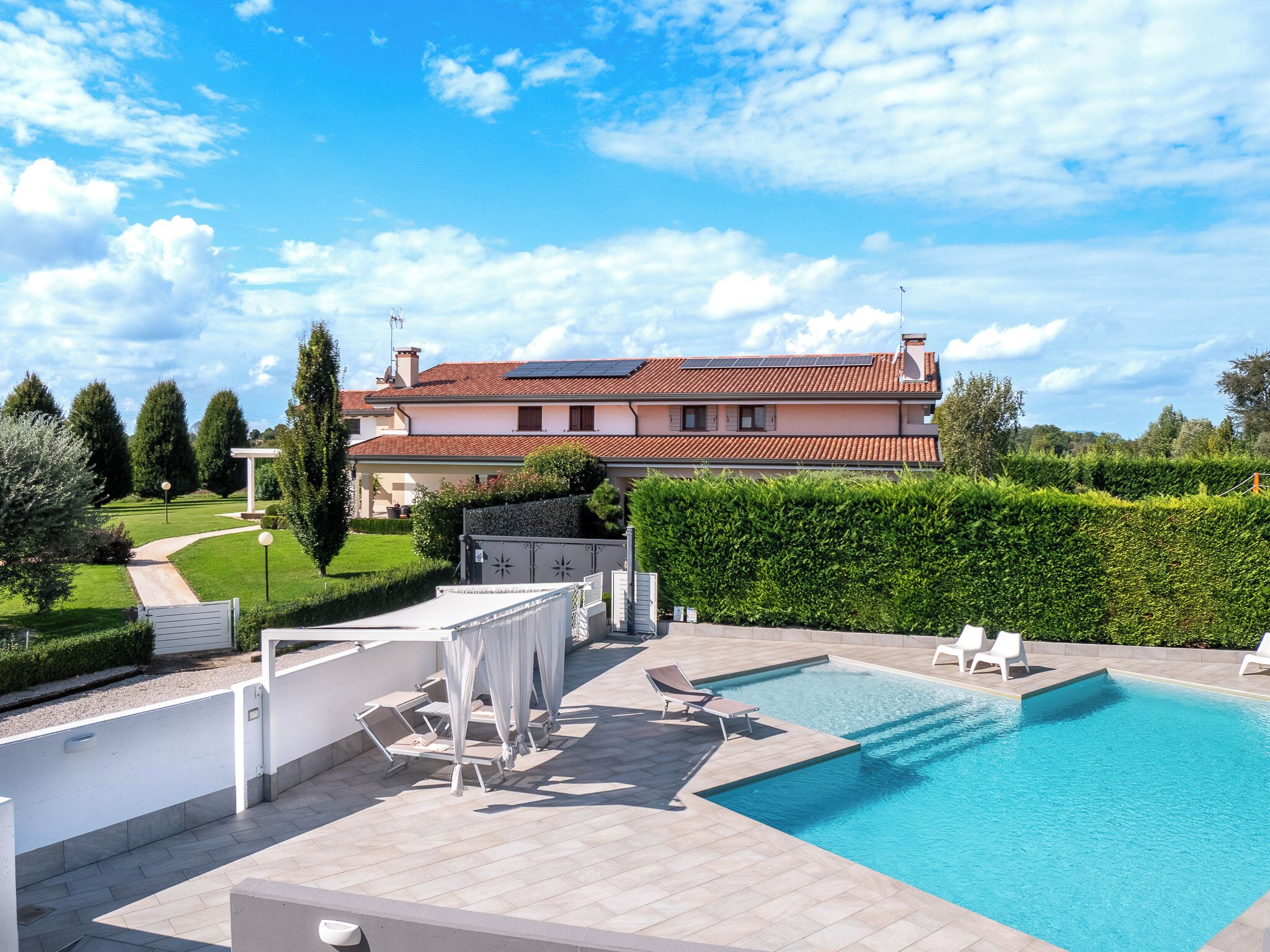 Una casa grande con piscina, mobiliario de exterior y un jardín bien cuidado.
