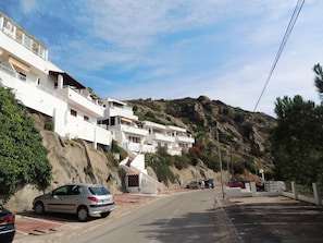 A residential area with white buildings, a road, and a hillside.