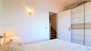 A bedroom with a bed, a nightstand, a lamp, a wardrobe, and a staircase leading to a landing. - Ibiza Bramer 27 Canyelles Roses - Barneda (Rosas / Roses)