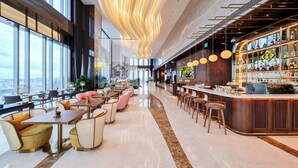 A modern bar area with a curved counter, seating with round tables and chairs, and large windows offering a city view.