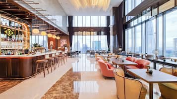 A modern bar area with a high ceiling and large windows offering a city view.