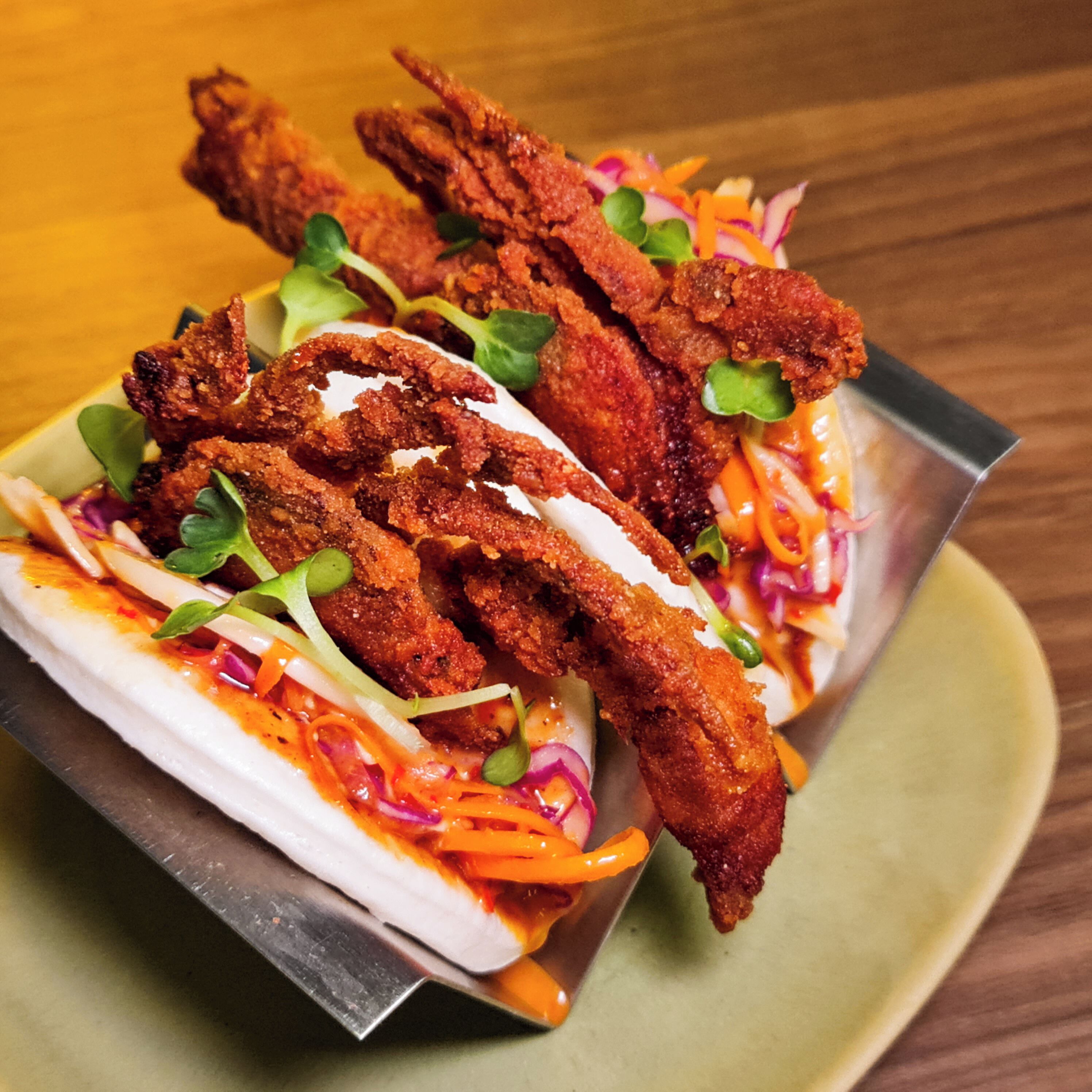 A dish with breaded chicken wings, coleslaw, and a creamy sauce on a metal plate.