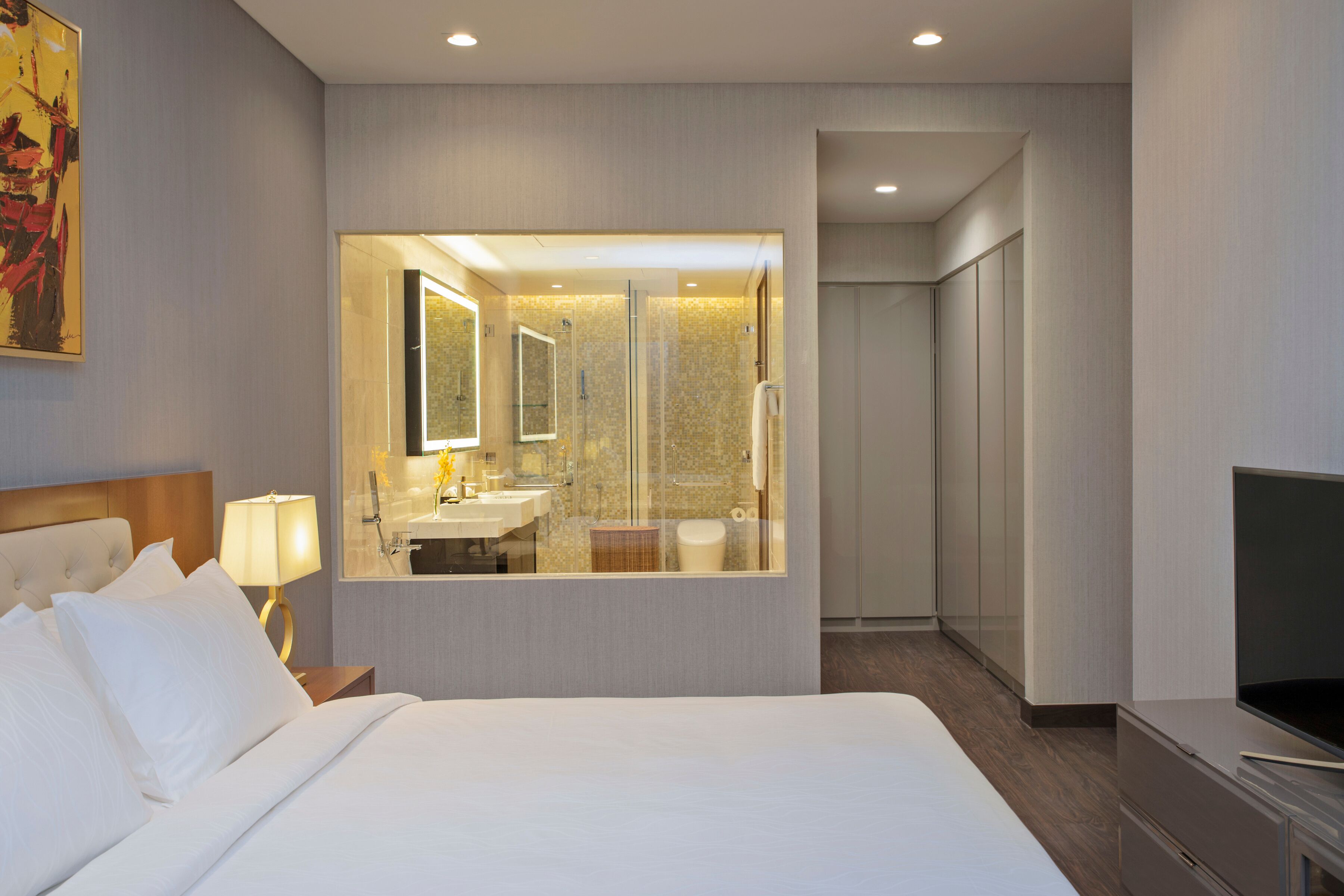 Una habitación de hotel con una cama grande, televisor, baño con espejo y vestidor.