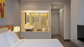 A hotel room with a large bed, a TV, a bathroom with a mirror, and a walk-in closet.