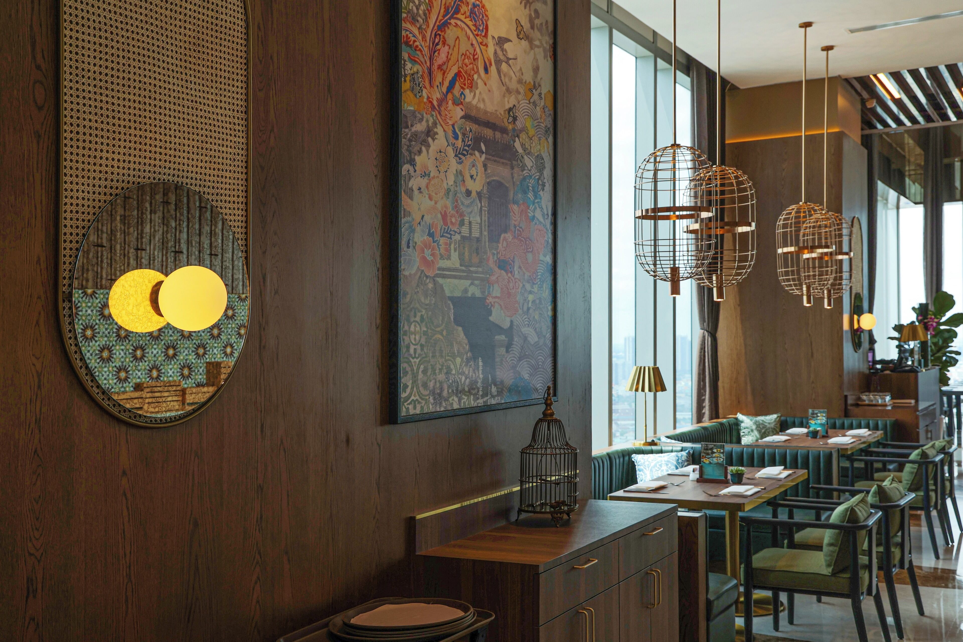 L’intérieur d’un restaurant présente des murs en bois, un grand tableau décoratif, des luminaires suspendus en fil métallique et un espace détente avec des tables et des chaises.