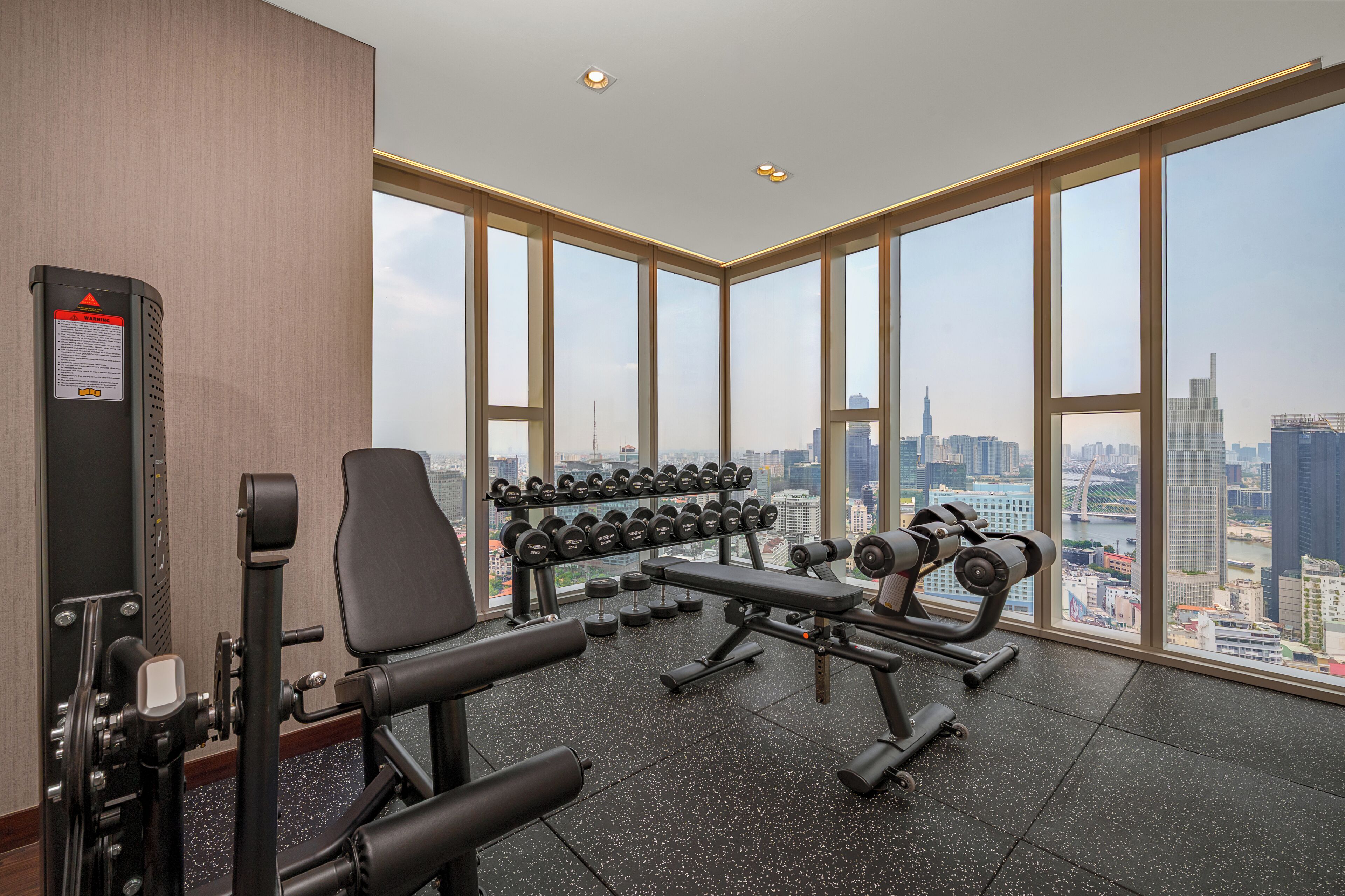 A gym with exercise equipment and large windows offering a city view.
