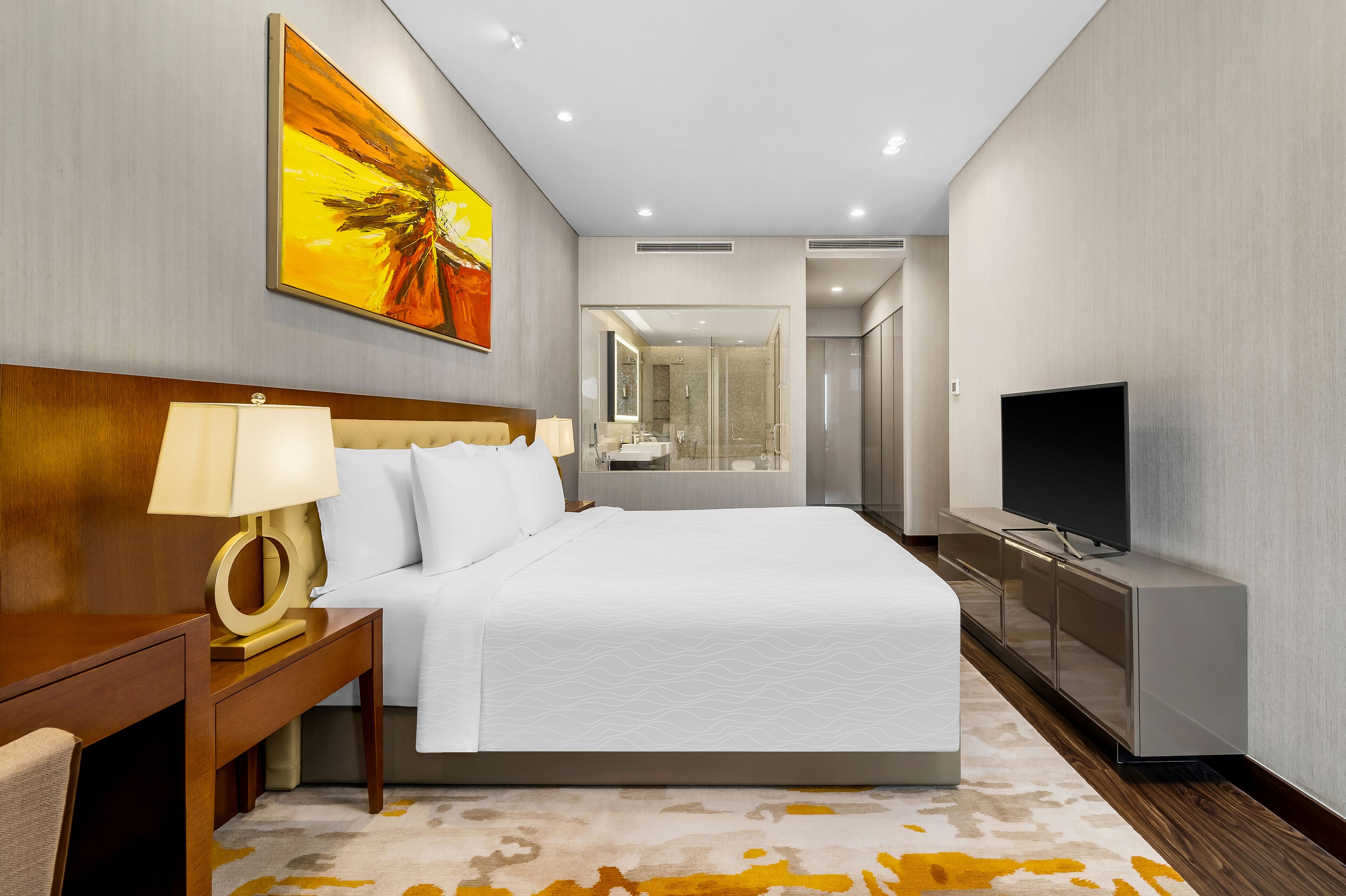 A modern hotel room with a large bed, bedside table with a lamp, a TV, and a painting on the wall.
