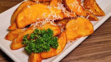 A plate of golden-brown potato wedges garnished with shredded cheese and parsley, accompanied by a small bowl of dipping sauce.