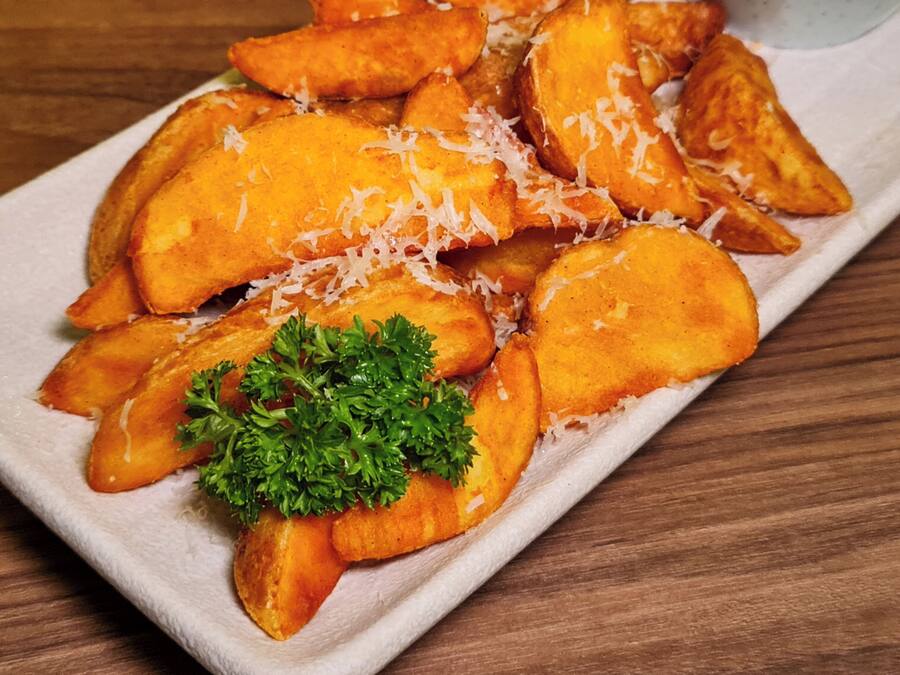 A plate of golden-brown potato wedges garnished with shredded cheese and parsley, accompanied by a small bowl of dipping sauce.