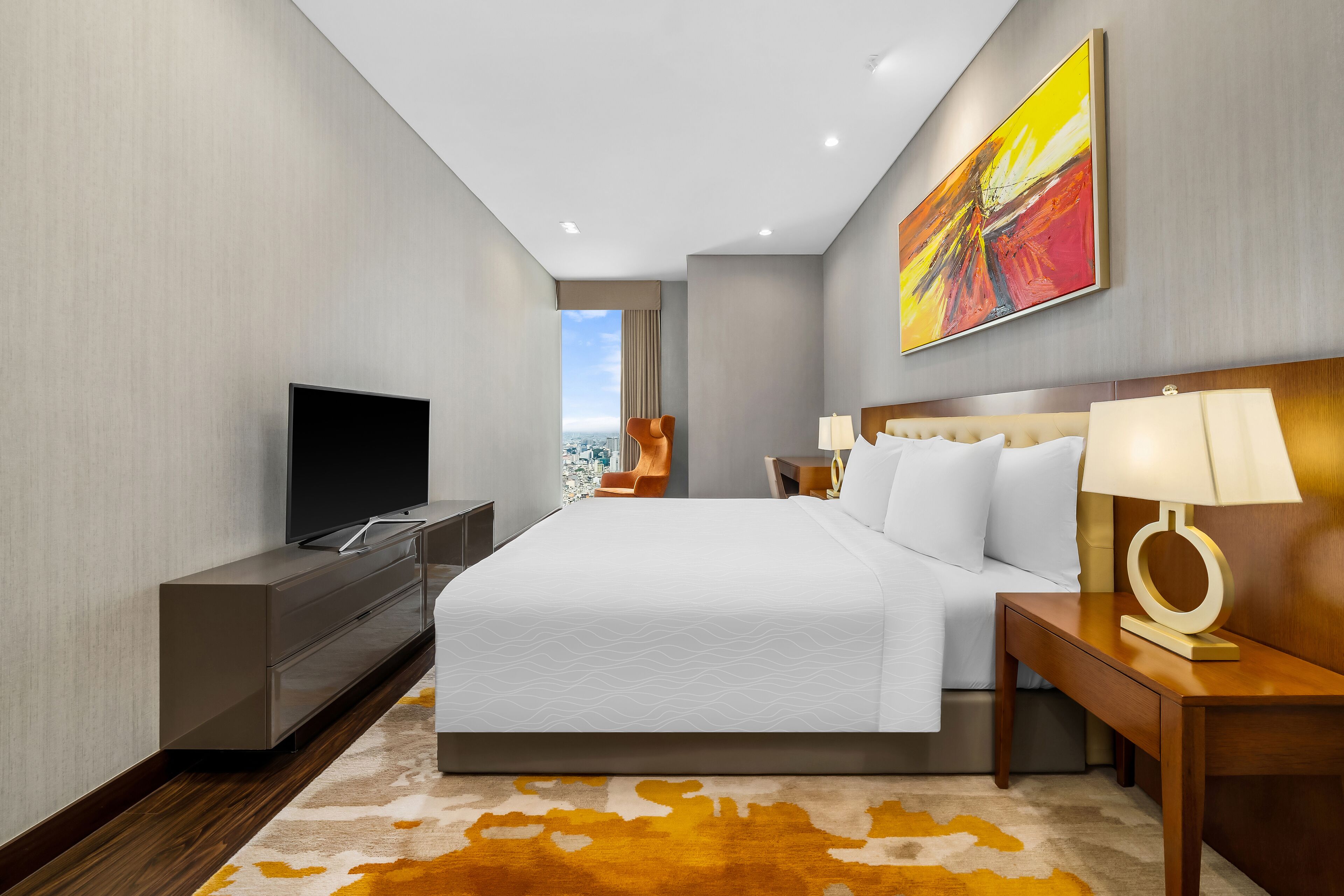 A modern hotel room with a large bed, a flat-screen TV, a desk, and a city view.