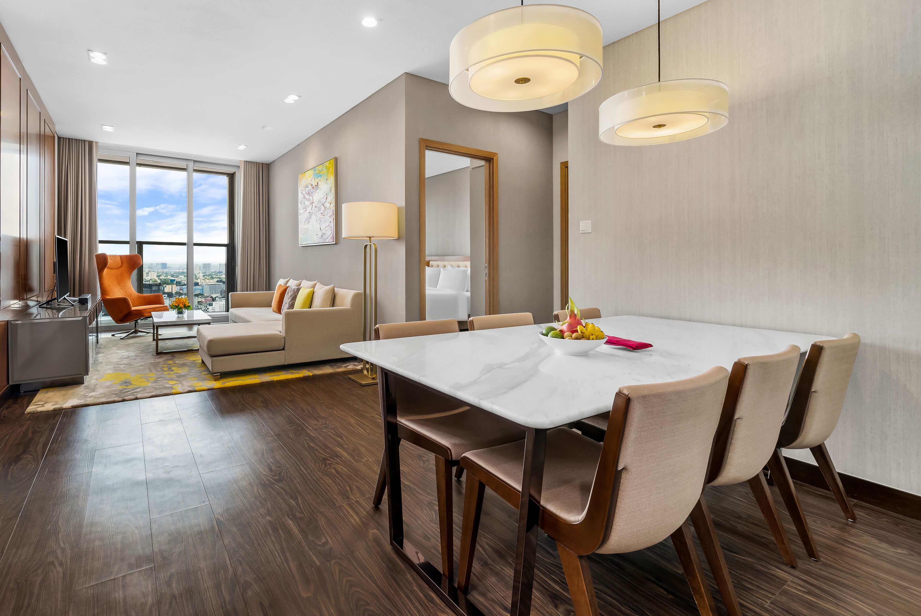 A modern hotel room with a dining area, a sofa, a large window with a city view, and a mirror.
