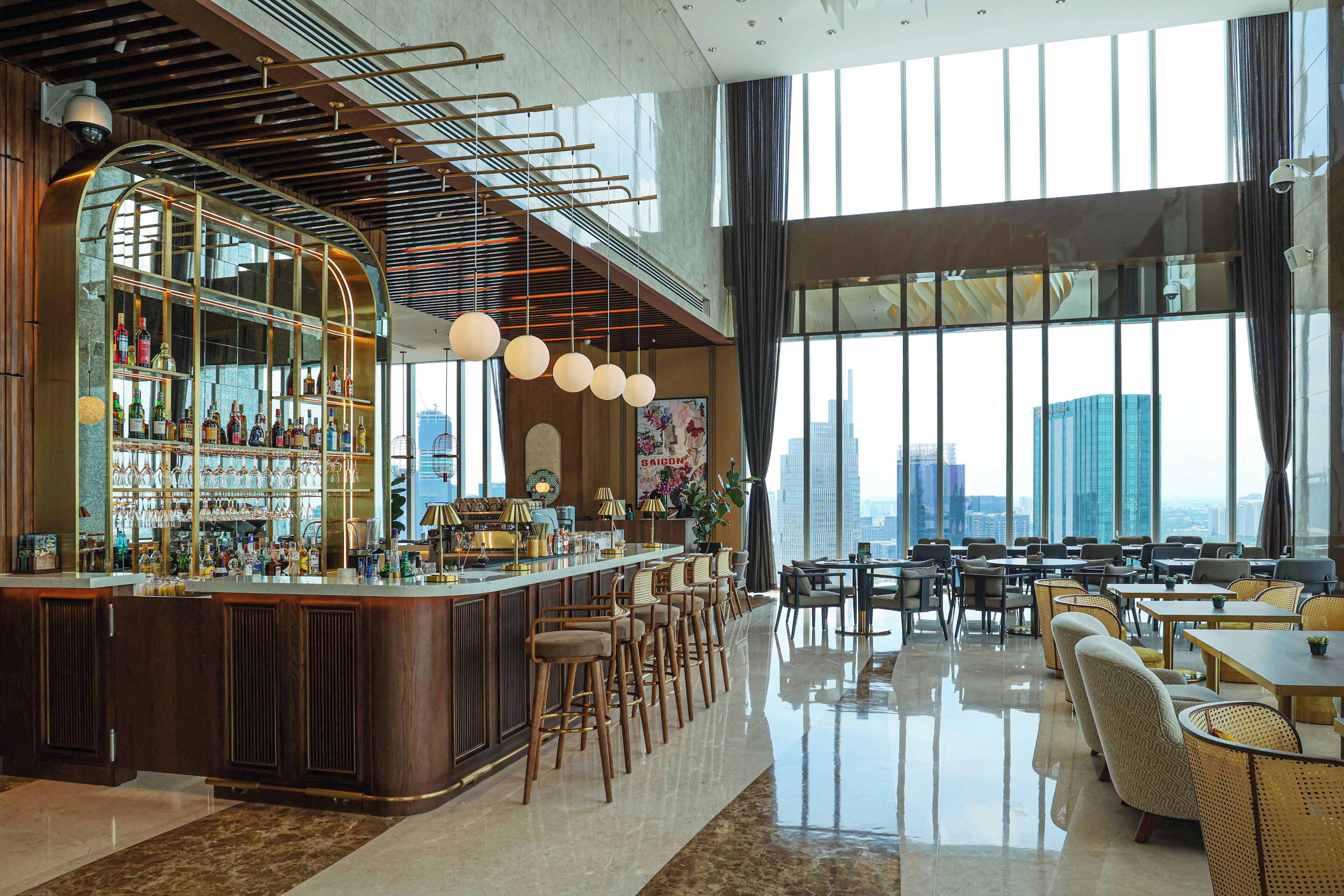A modern bar area with a curved counter, bar stools, and a city view through large windows.