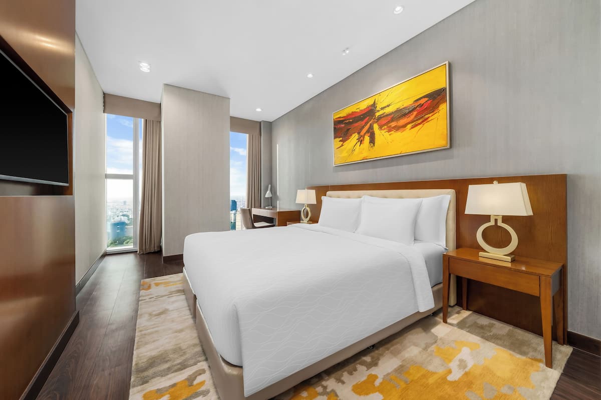 A modern hotel room with a large bed, a flat-screen TV, a desk, and a view of the city.